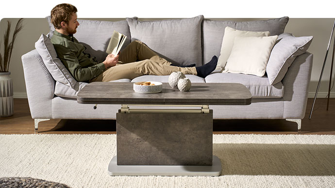Mann sitzt auf einem Sofa. Davor ein grauer Couchtisch.