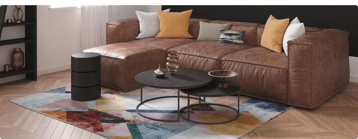 Wohnzimmer mit brauner Ledercouch, schwarzem Couchtisch, Dekokissen und mehrfarbigen Vintageteppich