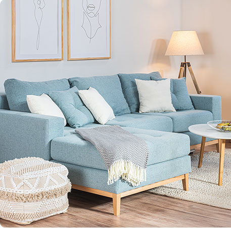 blaues Ecksofa mit Holzakzenten, Strickpouf, weißer Couchtisch mit Holzbeinen in einem Wohnzimmmer