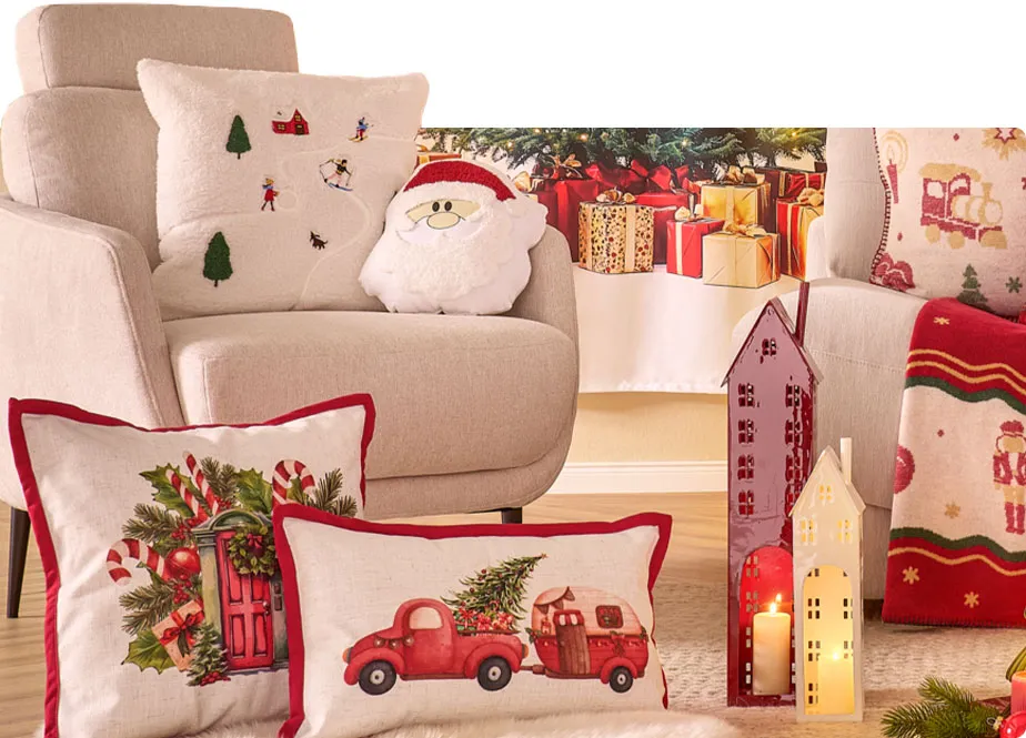 beiger Sessel mit weißem Kissen und Kissen im Weihnachtsmannmotiv, 2 cremefarbige Kissen mit rotem Keder und Weihnachtsdruck, rote und weiße Laterne in Hausoptik, rot-weiße-Weihnachtsdecke