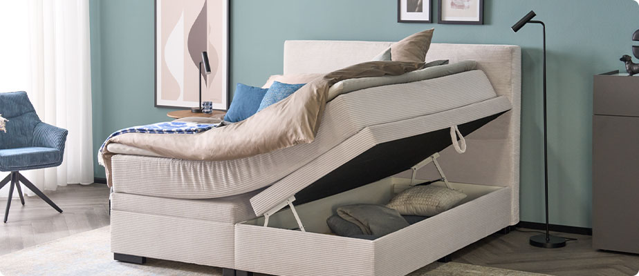 Schlafzimmer mit Boxspringbett in Creme, Cordbezug, Bettkasten rechts aufegklappt