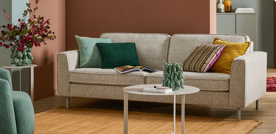 Wohnzimmer mit grauem Sofa, Kissen in Grün, Senf und mit Streifenmuster, weißer Couch- und ein Beistelltisch, grüne Vasen mit 3D Muster mit Avocados und Chilischoten