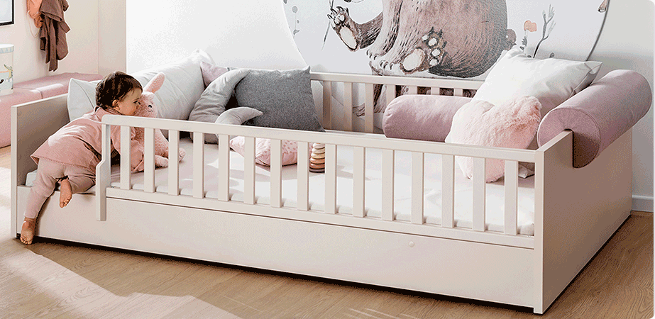 Babyzimmersituation mit beigem Babybett. Ein Kleinkind klettert durch den Einstieg