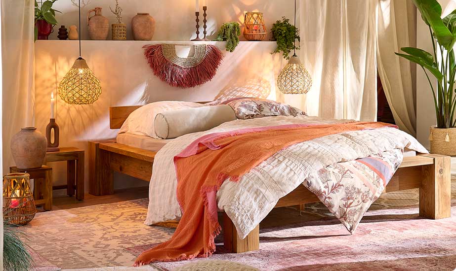 Schafzimmer mit massivem Holzbett, Bettwäsche in Creme und mit floralem Muster, Orientteppich, Deckenleuchten aus Rattan, Kerzenhalter und Vasen aus Rattan und Steinzeug