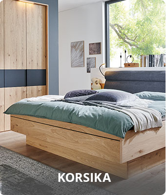 Korsika - Schlafzimmer mit Bettanlage aus Holz mit gepolstertem Kopfteil in Grau und grauen Absetzungen an der Nachtkommode - Holzschrank mit grauer Akzent - im Hintergrund ein großes Fenster