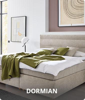 Dormian - Schlafzimmer mit beigem Boxspringbett mit weißem Bettzeug und khakigrüner Tagesdecke