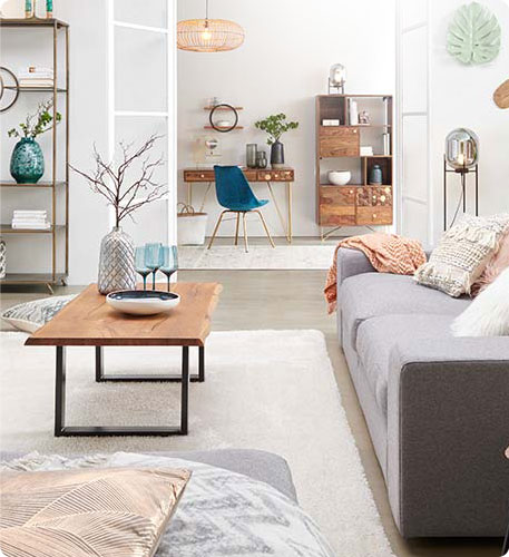 grauer Hocker mit Kissen und Decke, grauer Sofa, Holzcouchtisch mit schwarzem Metallgestell, weißer Teppich, weitere Möbel in einem Wohnzimmer