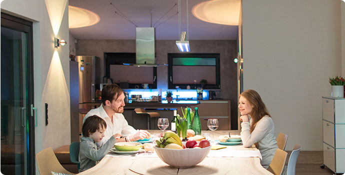 Esszimmer, Hintergrund Küche: Familie (Mutter, Vater, Kind) sitzt beim Essen am Küchentisch. Verschiedene Lichtfarben sorgen für unterschiedliche Effekte.