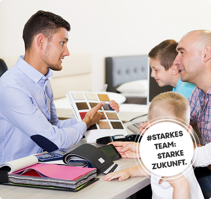 Auszubildender im Beratungsgespräch mit einer Familie. Er hält eine Farbpalette in der Hand. Drumherum Stoffmuster.