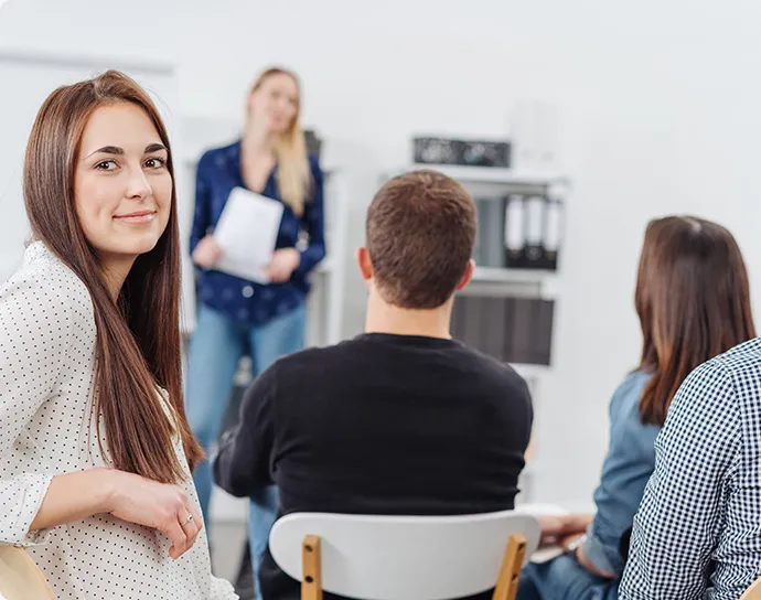 Auszubildende im Klassenraum, Sitz auf einem Stuhl und schaut nach rechts über die Schulter.