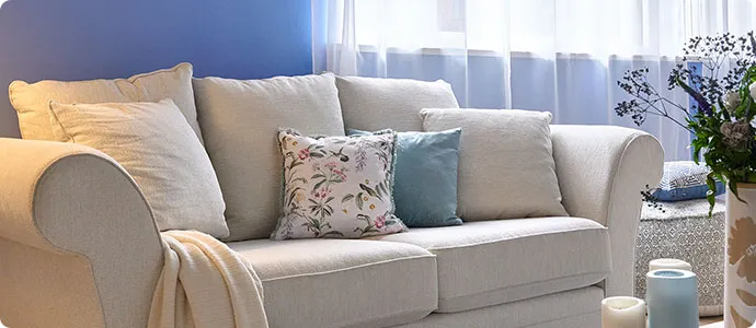Wohnzimmer mit hellgrauem Sofa, Kissen und Decke, blaue Wand, Deko