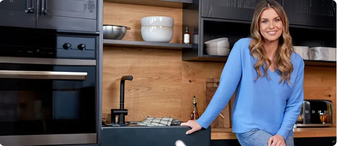 Schwarze Küche mit Holzrückwand. Laura Wontorra stützt sich auf die Arbeitsplatte.