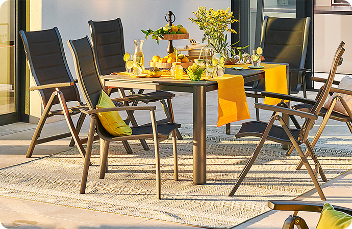 gedeckter Gartentisch und Gartenstühle, im Vordergrund eine Gartenliege am Pool