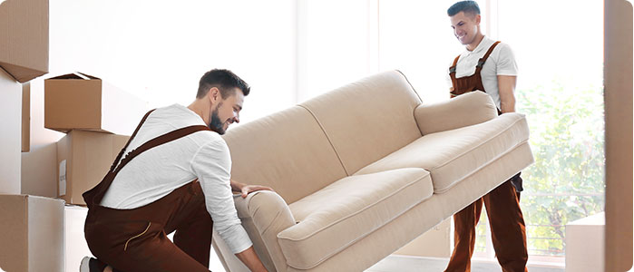Zwei Männer tragen ein Sofa. Im Hintergrund sieht man Kartons.
