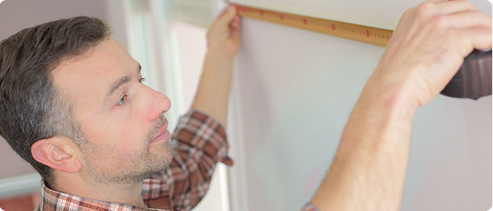 Ein Mann misst mit einem Zentimetermaß eine Wand aus.