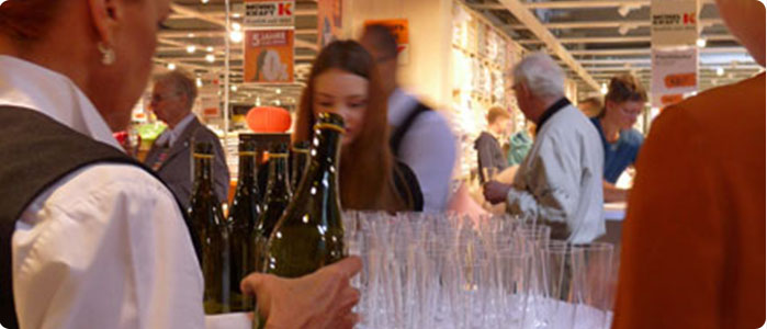 Viele Personen in einer Ausstellung. Es wird Sekt ausgeschenkt.