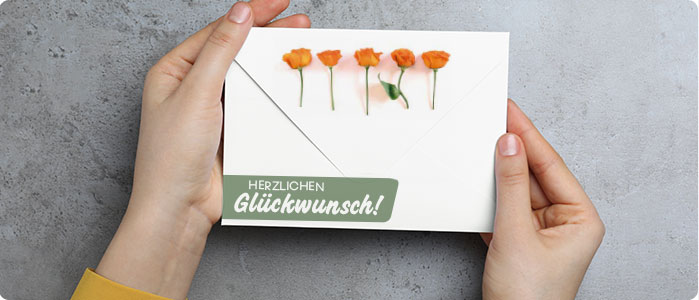 Ein Briefumschlag wird von 2 Händen gehalten. Auf dem Briefumschlag sind 5 Rosen und der Text Herzlichen Glückwunsch