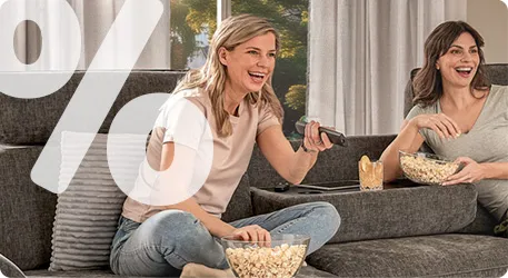 Zwei Frauen sitzen auf der Couch und essen Popcorn. Rechts oben in der Ecke ist ein Prozentzeichen
