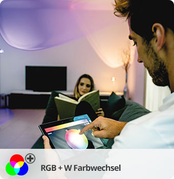 RGB + W Farbwechsel, Mann hält ein Tablett mit geöffneter App-Funktion zum Farbwechsel vor sich. Im Hintergrund sitzt eine Frau und liest