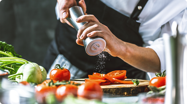 Koch streut Salz über Tomaten