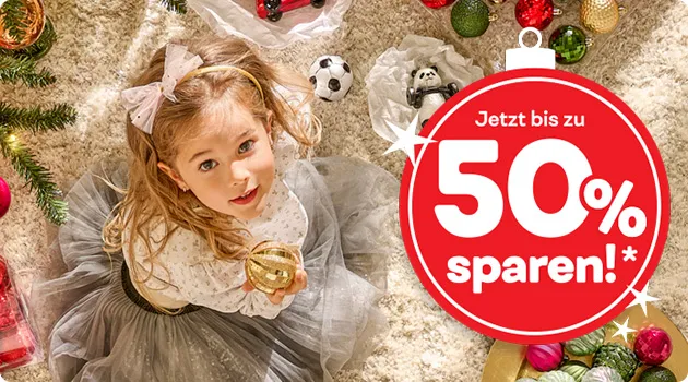 Mädchen sitzt auf dem Teppichboden, schaut nach oben und hält eine goldene Weihnachtskugel in der Hand. Ringsherum Baumschmuck in Rot, Grün, Gold und Creme. Text: Jetzt bis zu 50% sparen*!