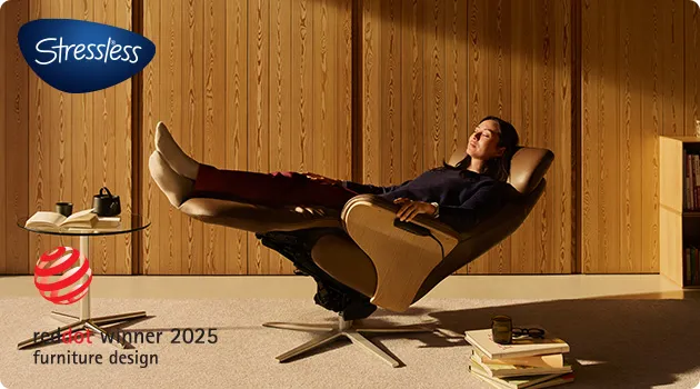 Frau liegt in einem braunen Relaxsessel, Logo Stressless, Logo reddot winner 2025 furniture design