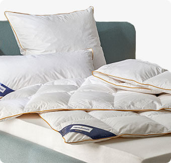 Weiße Bettdecken und Kissen von Heidelberger Bettwaren auf einem grauen Bett