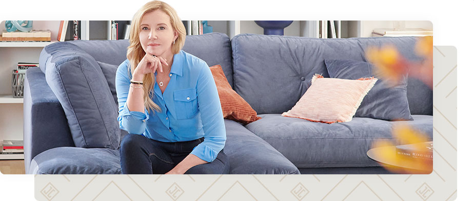 Designerin Jette Joop sitzt auf blauem Sofa in einem Sofa - Jette Home Muster in Creme und Beige im Hintergrund 