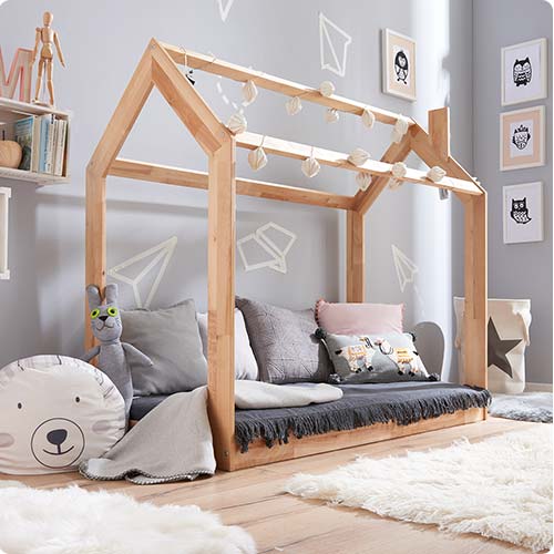 Kinderzimmer mit Haus-Spielbett aus Holz mit sehr vielen Kissen und einer Lichterkette geschmückt.