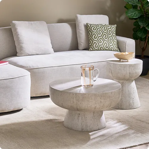 cremefarbiges Ecksofa mit grün-beige gemusterten Kissen, runde Couchtische in Steinoptik, Deko