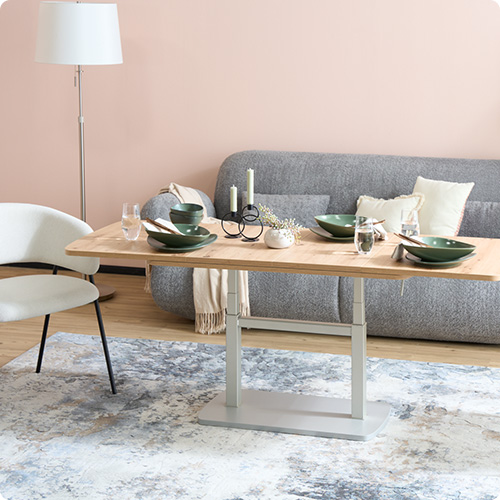 Wohnzimmer mit höhenstellbaren Couchtisch, grauem Sofa und 2 weißen Stühlen.