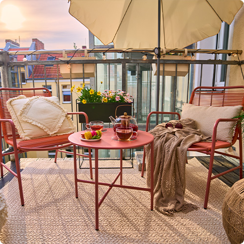 Balkon mit Gartenmöbeln, 2 Stühle und 1 Tisch in Terracottagfarben und Sonnenschirm in Beige. Hintergrund Häuserkulisse.