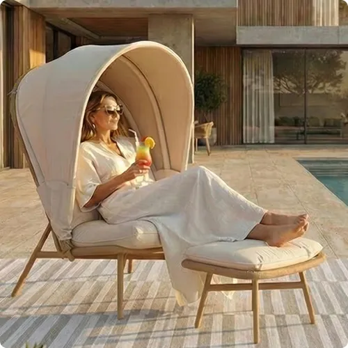 Frau sitzt auf einem Lounge-Sessel mit Sonnendach und hat die Füße auf einem Hocker liegen. Sie hält ein Getränk in der Hand.