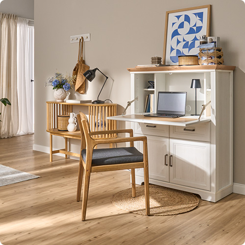 Wohnzimmer mit weißem Sekretär mit Holzakzenten im Landhausstil, Holzstuhl und Holz-Kommode vor beiger Wand, Deko