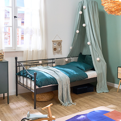 Schwarzes Metallbett mit hellgrünem Betthimmel, petrolfarbiger Bettwäsche und hellgrünem Plaid, Deko und Spielzeug in einem Kinderzimmer