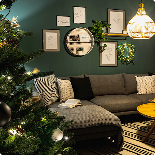 Weihnachtsbaum, graues Ecksofa mit Kissen in Schwarz-Weiß, Rattanpendelleuchte und Wanddeko in einem Wohnzimmer
