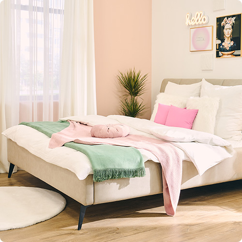 beiges Bett mit weißer Bettwäsche, rosa Kissen und hellgrüner Decke in einem Schlafzimmer