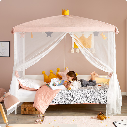 Weißes Kinderbett mit Baldachin in Weiß und Rosa mit gelbem Krönchen, lesendes Mädchen in Bett, Bettwäsche, Kissen, Spielzeug und Deko