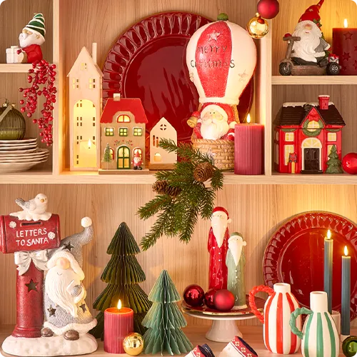 Regal mit Weihnachtsdeko: Weihnachtsmann mit Briefkasten und Aufdruck Letters to Santa, rote LED-Kerze, Papier-Tannenbäume in Grün, Keramik-Weihnachtsmänner in Rot und Grün, beleuchtete Häuschen, Tannenzweige, Weihnachtsmann in Heißluftballon