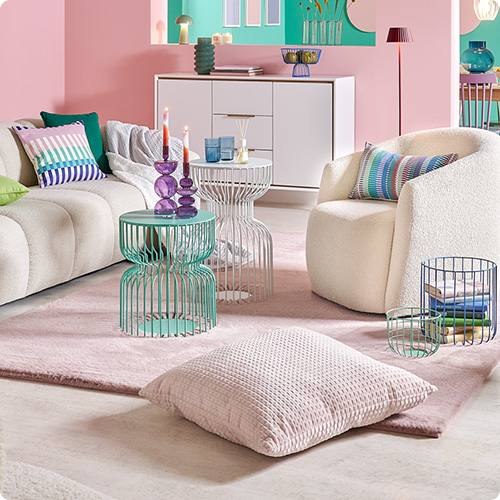 Wohnzimmer mit weißem Sofa, weißem Sessel und weißer Kommode, Metall-Couchtische in Mintgrün und Weiß, Textilien und Deko in Pastelltönen, rosa Wände