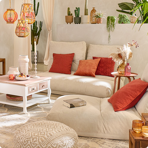 Wohnzimmer mit zwei beigen Relaxliegen, terrakotta-farbene Kissen, Bodenkissen in Creme, weißer Couchtisch mit holzfarbener Tischplatte, bunte und weiße Glas- und Keramikaccessoires