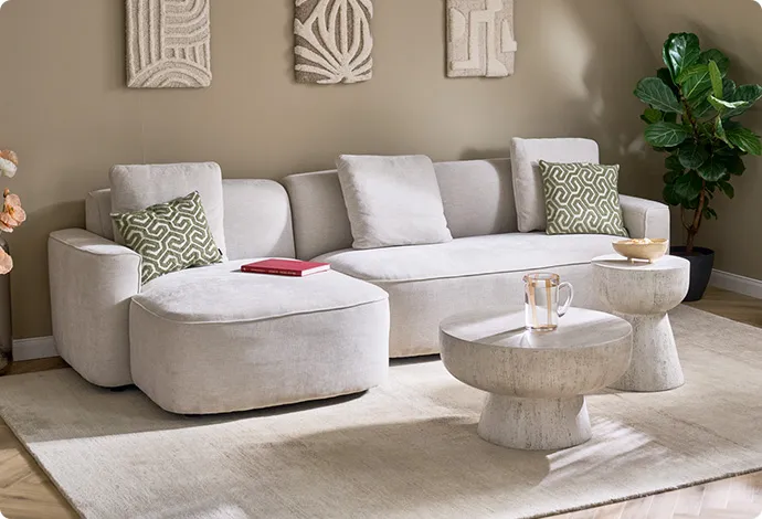 cremefarbiges Ecksofa mit grün-beige gemusterten Kissen, runde Couchtische in Steinoptik, Deko