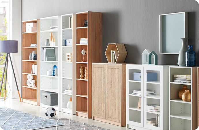 Weiße und 2 holzfarbige Regale mit Deko sowie eine Kommode in Holzoptik, vorne 2 Teppiche mit Rautenmuster und ein Fußball