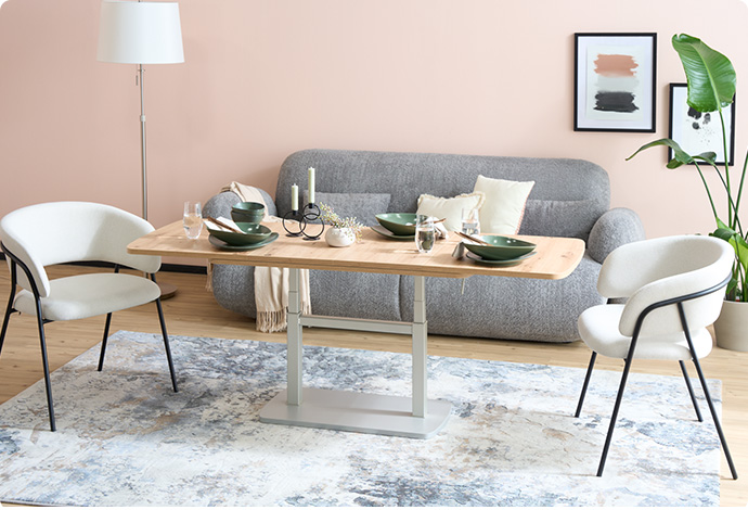 Wohnzimmer mit höhenstellbaren Couchtisch, grauem Sofa und 2 weißen Stühlen.