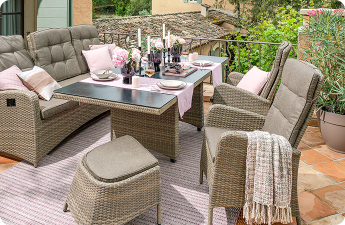 Gartensessel, Gartentisch, Gartensofa - alle in Beige und aus Polyrattan mit passenden Auflagen auf einer Terrasse - Tisch ist gedeckt