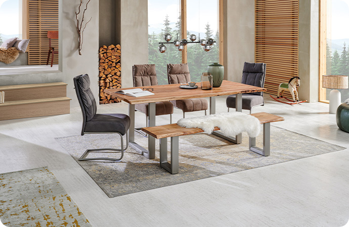 Esszimmer mit zentraler Essgruppe, bestehend aus Esstisch, Bank und Polsterstühlen - Esstisch und Bank mit Platten aus Echtholz und Edelstahlgestell in U-Form - auf der Bank liegt ein weißes Fell, auf dem Tisch sind ein aufgeschlagenes Buch, Vasen und andere Deko platziert