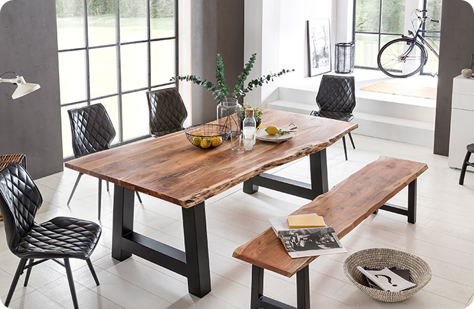 Esszimmer mit Draufsicht auf Holztisch und passende Holzbank, beide mit schwarzen Gestellen. Polsterstühle in Anthrazit mit Steppung, Deko