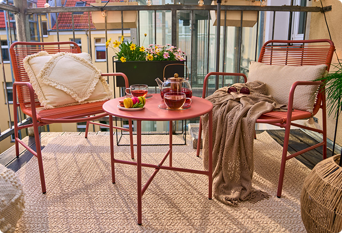 Balkon mit Gartenmöbeln, 2 Stühle und 1 Tisch  in Terracottagfarben und Sonnenschirm in Beige. Hintergrund Häuserkulisse.