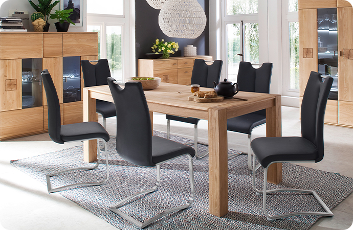 Esszimmer mit Essgruppe bestehend aus Holz-Esstisch und dunkelgrauen Freischwingern, im Hintergrund beleuchtete Stauraummöbel aus Holz, wie Highboard, Kommode und Vitrine