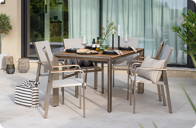 Gedeckter Gartentisch aus Aluminium mit Tischplatte in Teakoptik sowie 6 Stühle aus Aluminium mit Textilgewebe auf einer Terrasse